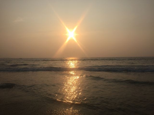 A sun setting into the sea. The sky is orange and we can see the sun's reflection in the sea.