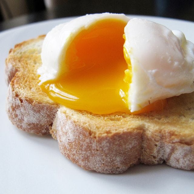 a single poached egg on artisan hand sliced toasted bread the egg is split to reveal a runny yolk
