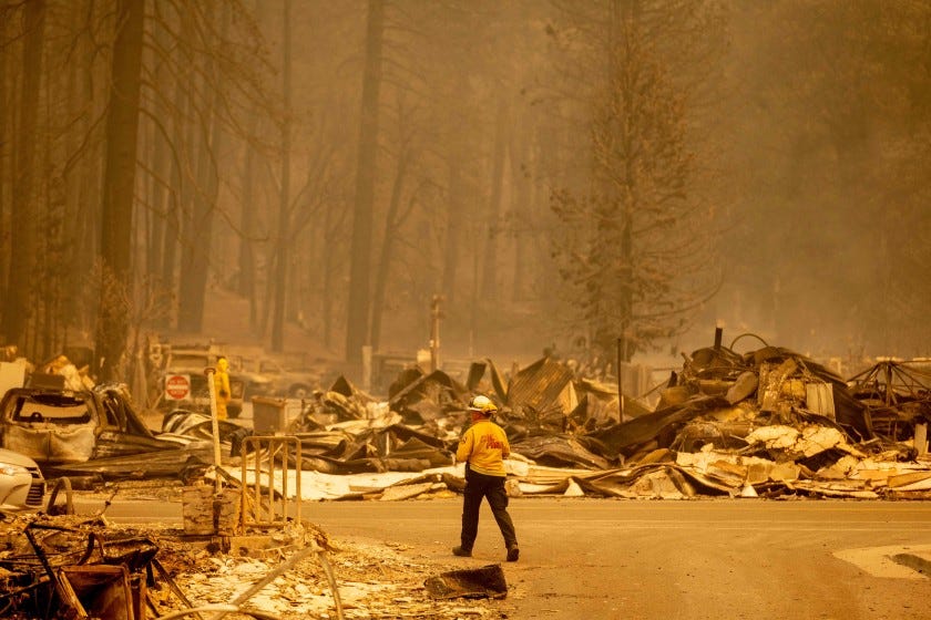 A firefighter walks through burned wreckage amid orange smoky haze