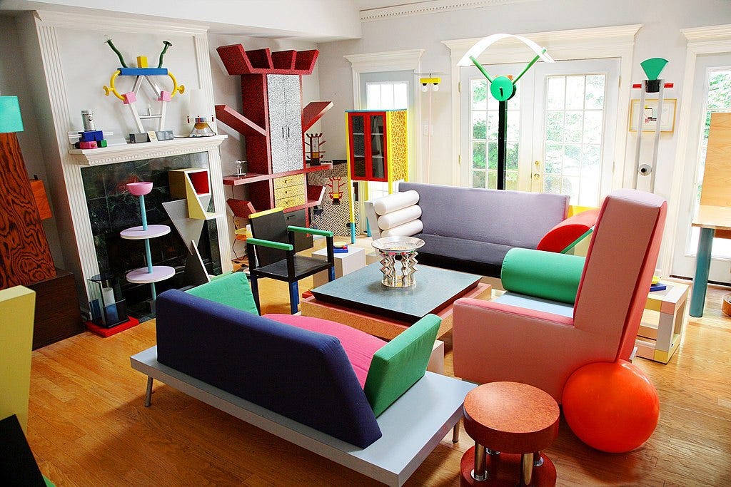 A living room furnished and decorated with brightly-colored chairs and couches in big geometric shapes and lots of furniture that looks like it came from a wealthy private nursery school. 