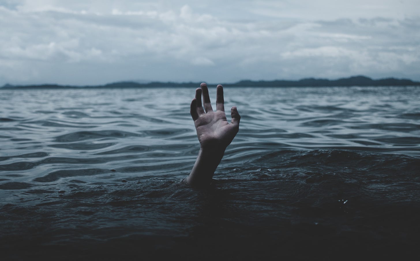 Photo of a single hand reaching out of dark waters on a gloomy lake.