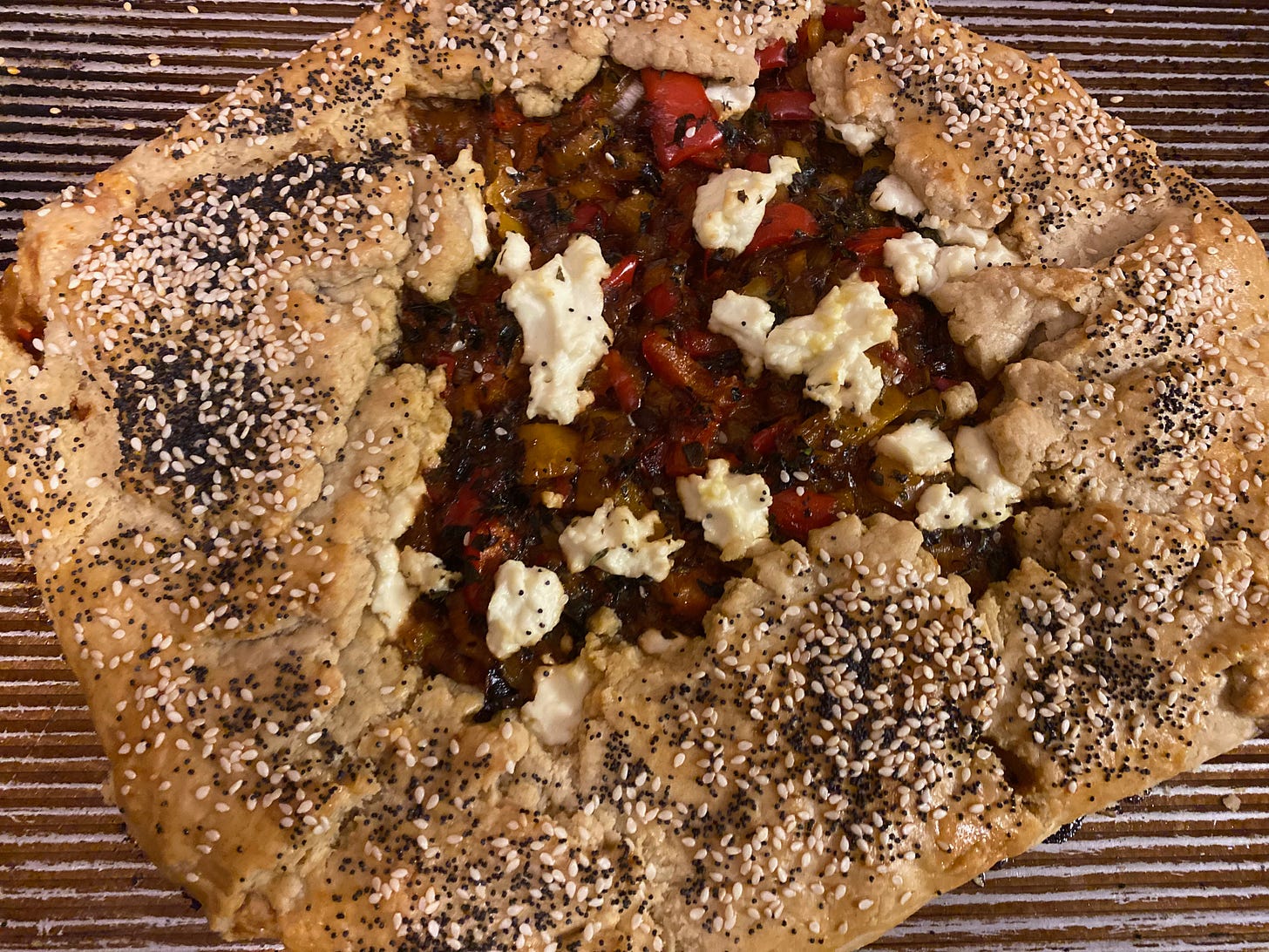 A red pepper galette covered in sesame and poppy seeds sits on a baking tray.