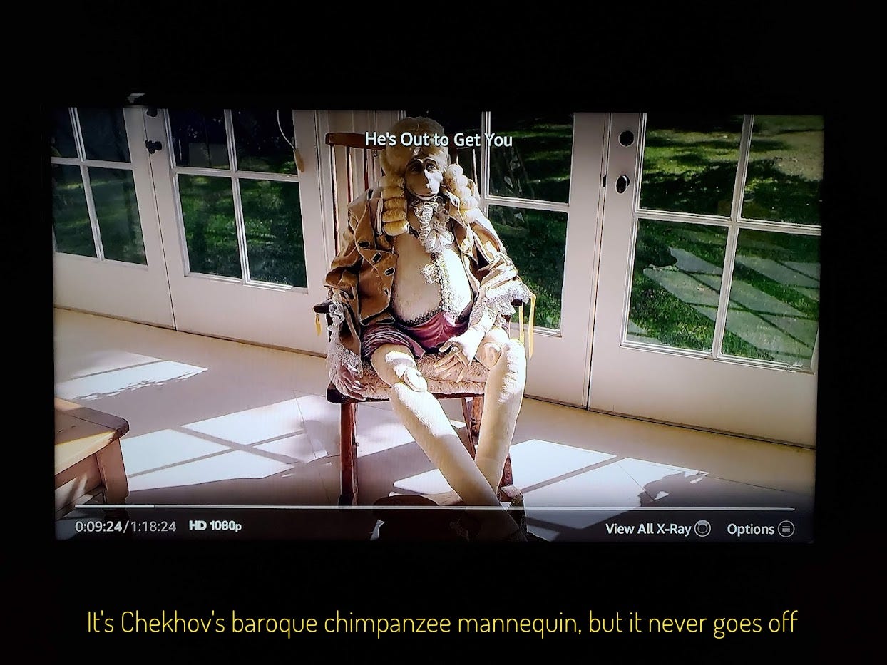 A life-sized mannequin in baroque clothes and wig, and chimpanzee face, in a rocking chair, captioned “It’s Chekov’s baroque chimpanzee mannequin, but it never goes off”