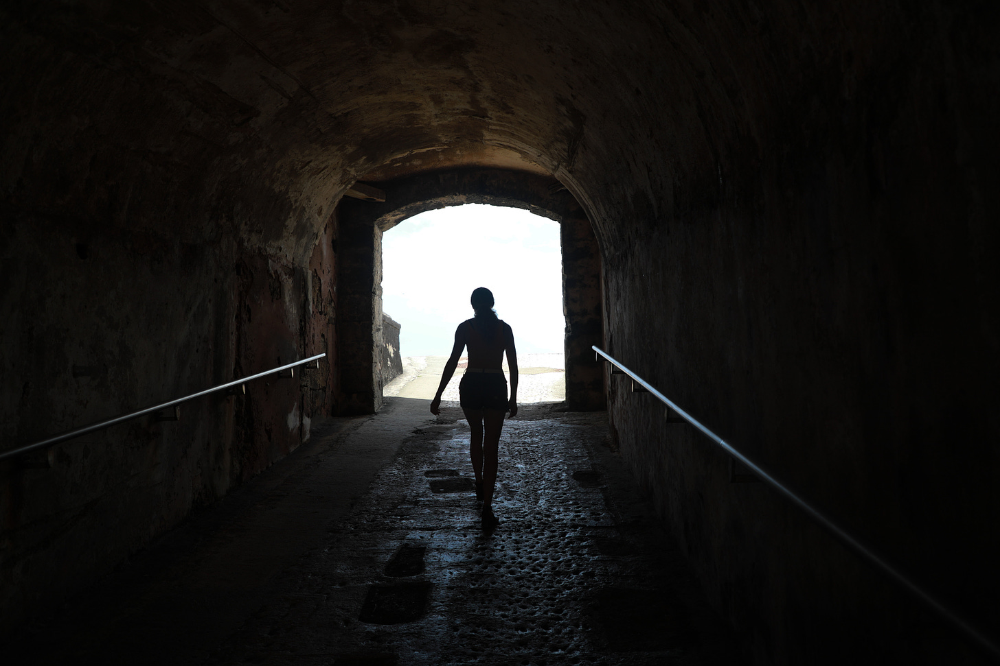 Woman is walking down a dark tunnel toward the light.