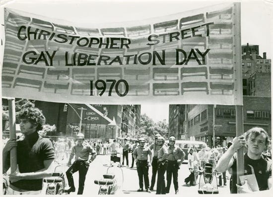Two people hold a banner reading CHRISTOPHER STREET GAY LIBERATION DAY 1970 as they walk away from police.
