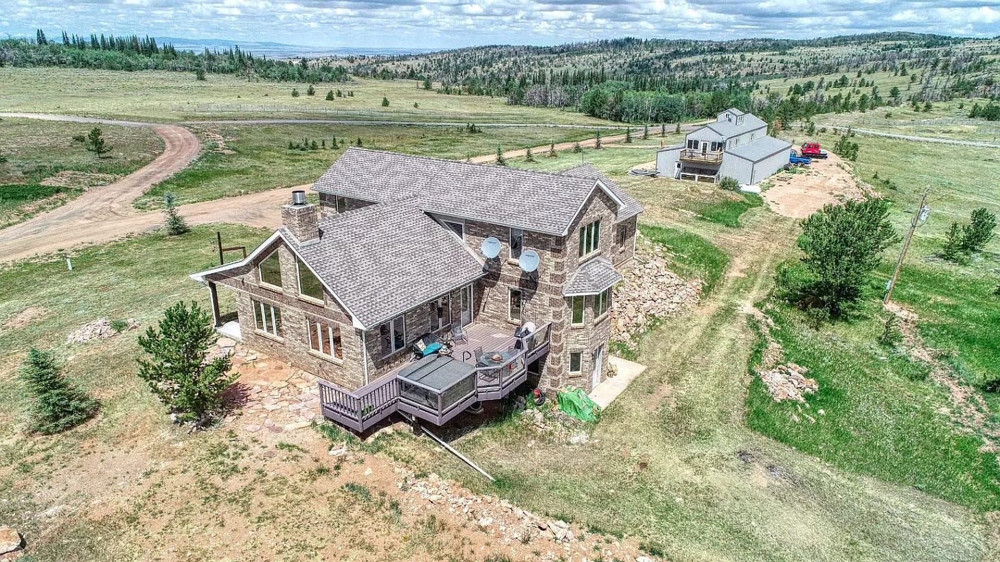 Aerial shot of a large brick home with an expansive back deck. Aside from the carriage house behind it, it's the only building visible for miles.