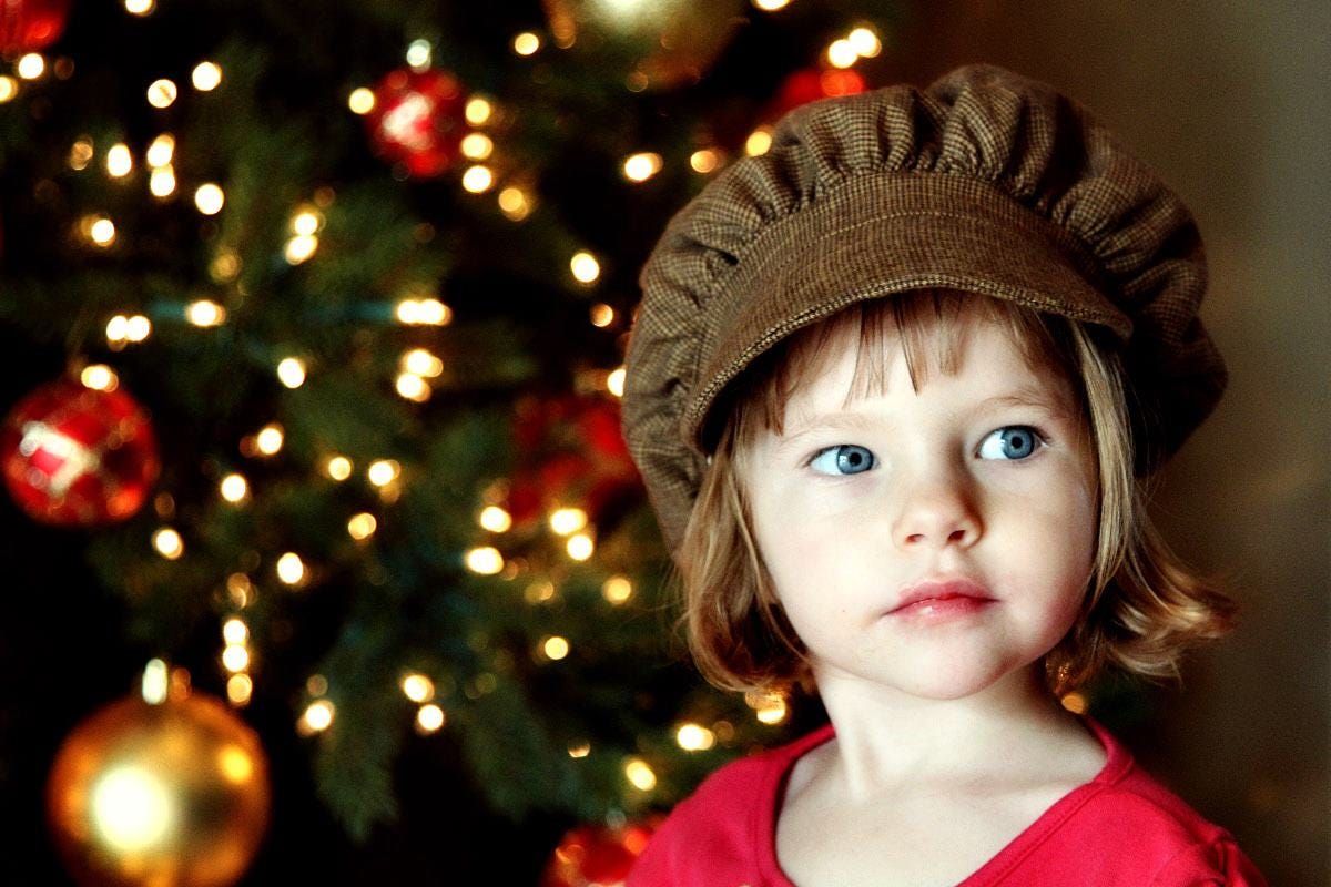 a young girl with blue eyes in a hat by a Christmas tree