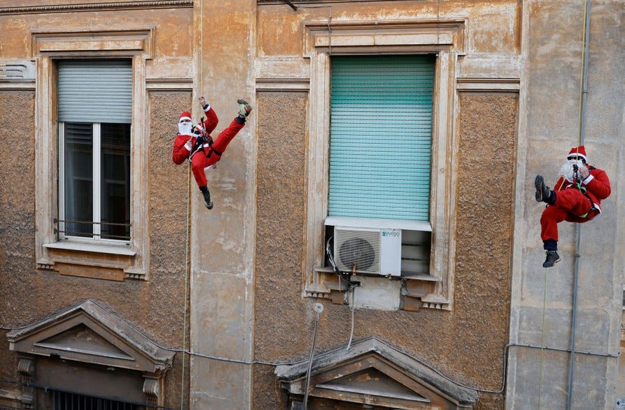Two people dressed as Santa Claus rappel down a building.