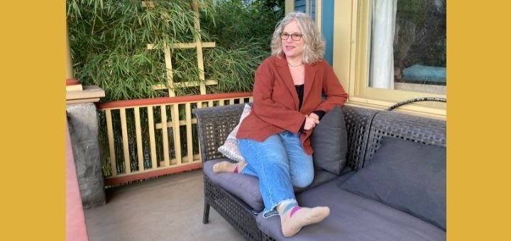 Woman in sweater, jeans, and sock sitting on a couch on a porch
