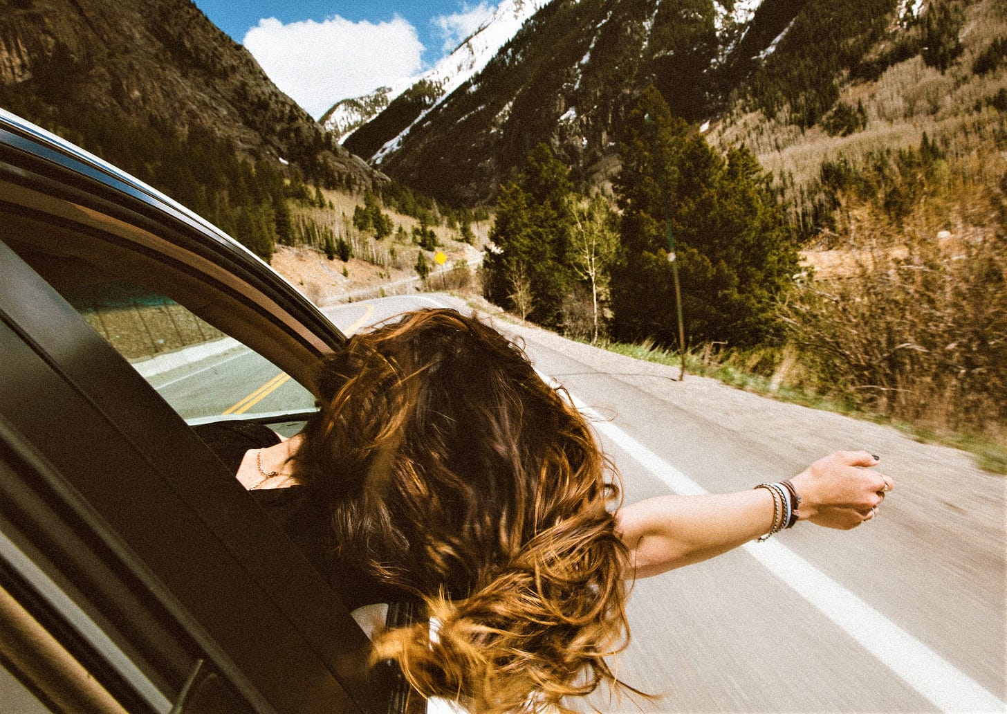 back view of girl with long brown hair with heaad and arm out car window looking forward back view of girl with long brown hair with heaad and arm out car window looking forward