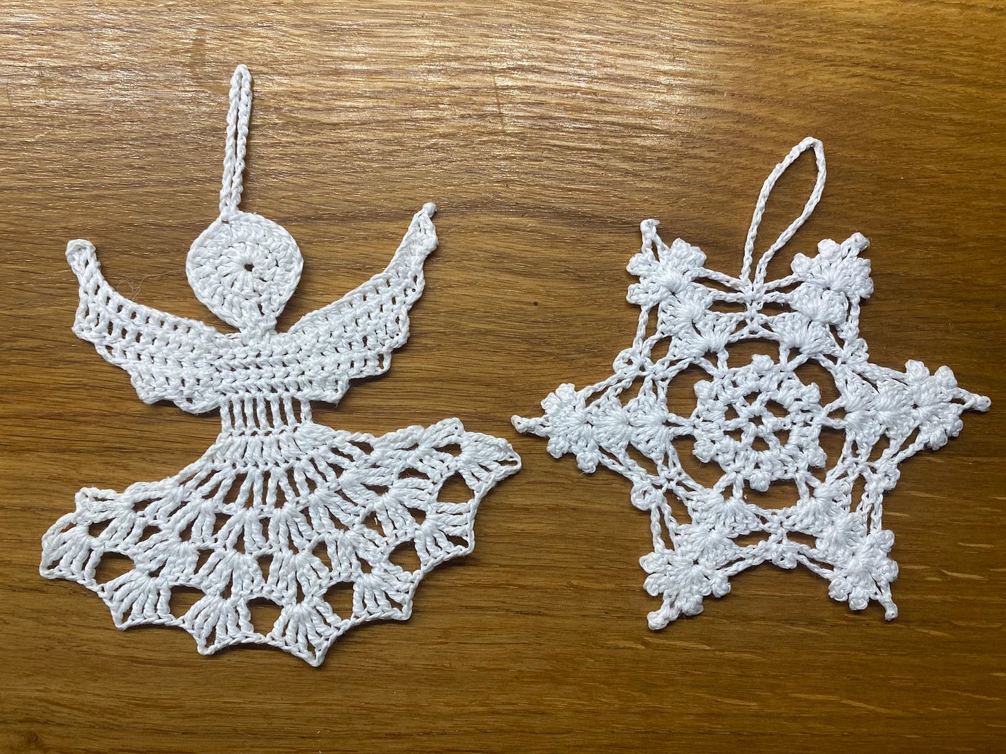 Handmade white christmas tree ornaments of an angel and a snowflake against a wooden table.