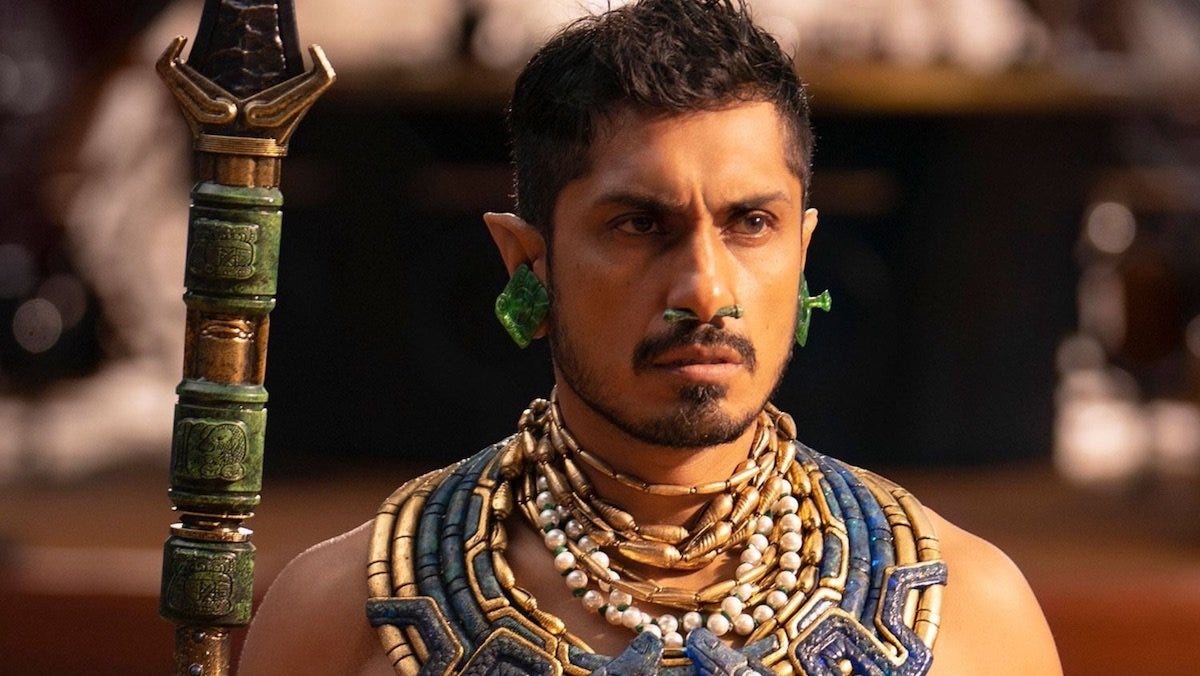 Actor Tenoch Huerta wearing jade and pearl jewelry and carrying a spear, in costume as Namor in the movie Wakanda Forever.