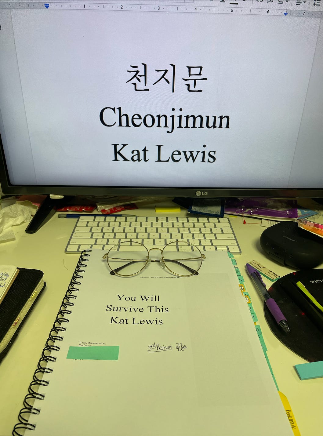 A photo of Kat’s printed manuscript and computer monitor. The monitor displays her old novel title, “CheonJiMun,” and the print out shows her new title, “You Will Survive This.”