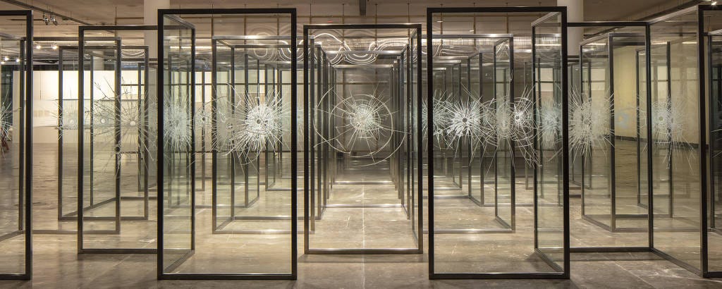 obra "Paisagem", de Regina Silveira. A obra é um labirinto de vidro com impressões brancas simulando estilhaços de marcas de tiro com buracos no meio.