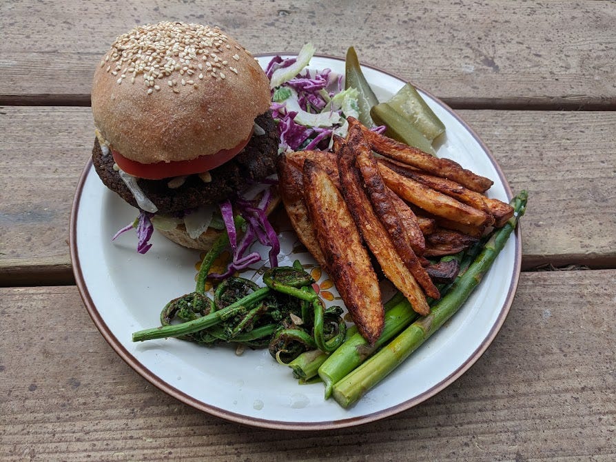 a plate with a black bean burger on a bun, roasted asparagus and fiddleheads, baked russet potato spears, cabbage slaw and a pickle - phew! a plate with a black bean burger on a bun, roasted asparagus and fiddleheads, baked russet potato spears, cabbage slaw and a pickle - phew!