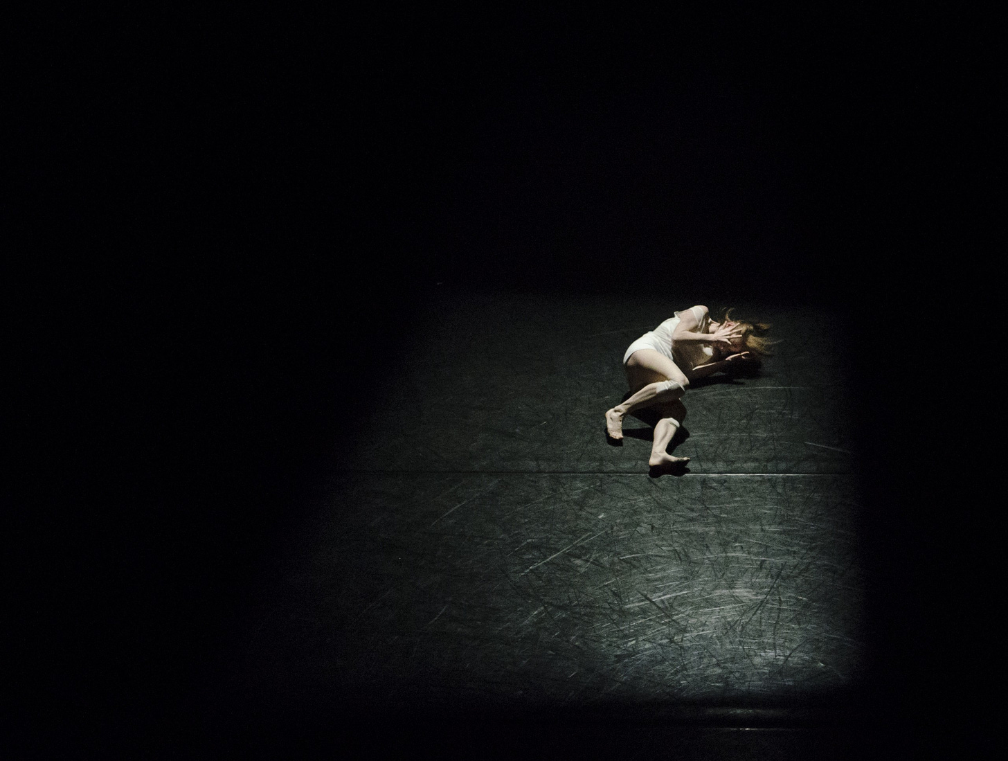 image of an actor lying on a black stage holding her head