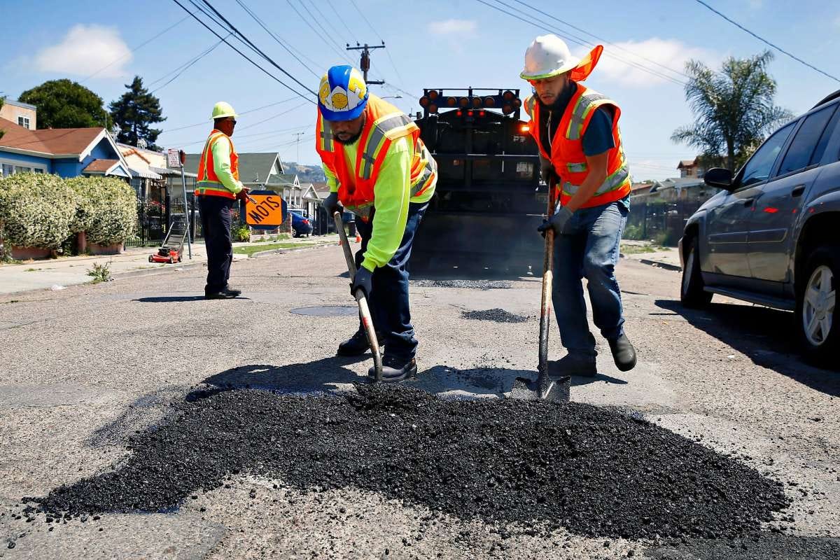 Photo of workers in orange vests filling a pothole in a residential neighborhood