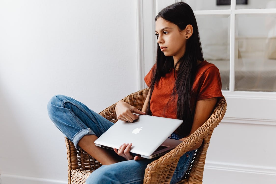 Girl Sitting on a Chair while Holding Her Laptop