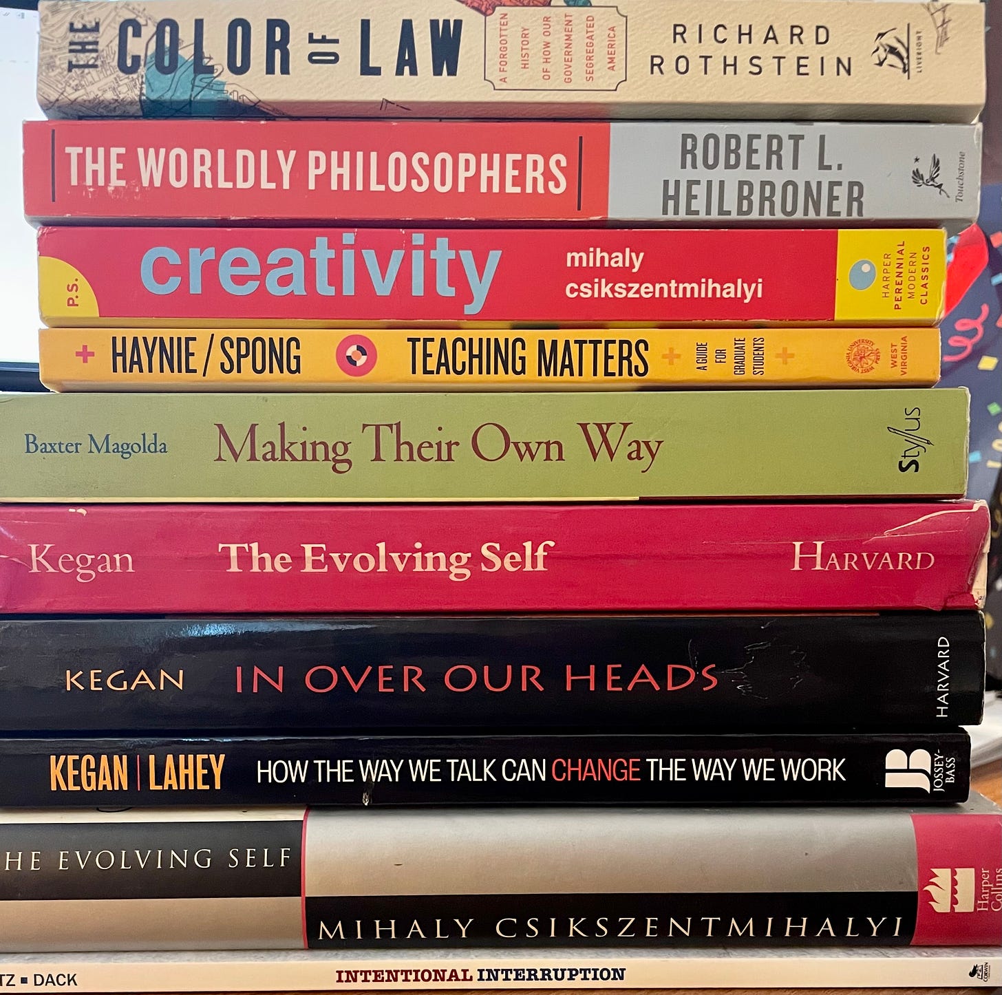 image of book spines; titles are the color of law, the worldly philosopers, creativity, making their own way, the evolving self by kegan, in over our heads, how we talk can change the way we work, the evolving self by czikszentmihalyi, intentional interruption