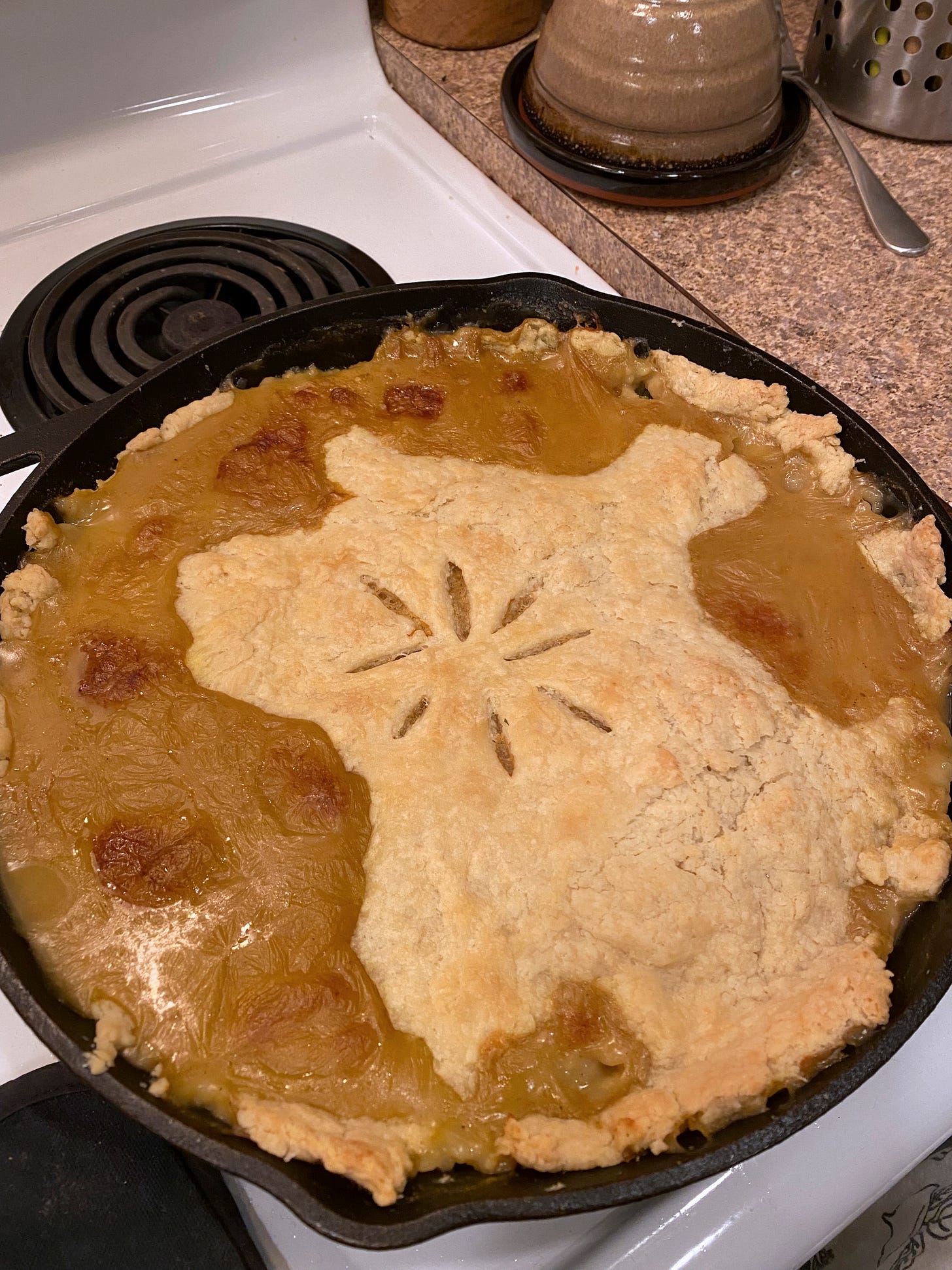 A cast iron pan with a pot pie, an asterisk shape scored in the centre. A brownish curried gravy has spilled overtop of the crust in several places.