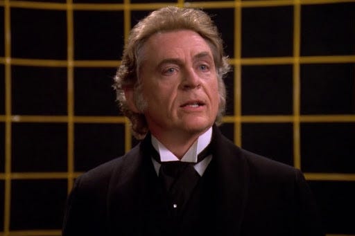 This image shows Professor James Moriarty (Daniel Davis) standing on the U.S.S. Enterprise-D's holodeck. Moriarty wears a Victorian English suit and addresses someone off-camera. This image shows Professor James Moriarty (Daniel Davis) standing on the U.S.S. Enterprise-D's holodeck. Moriarty wears a Victorian English suit and addresses someone off-camera.