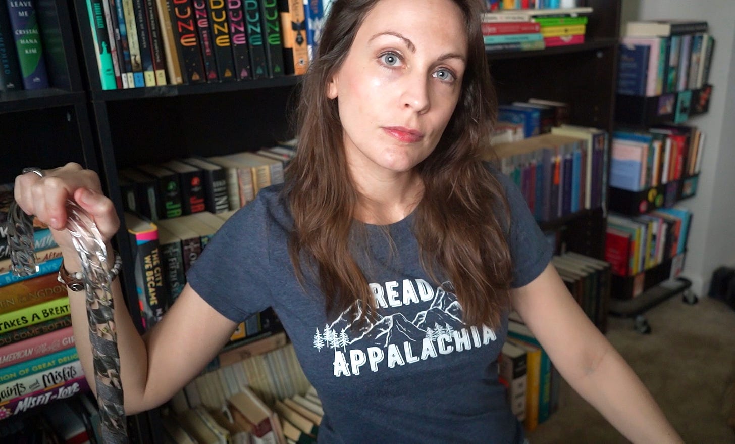 a photo of Kendra, a white woman with brunette hair, wearing a Read Appalachia t-shirt and holding a cane in here right hand