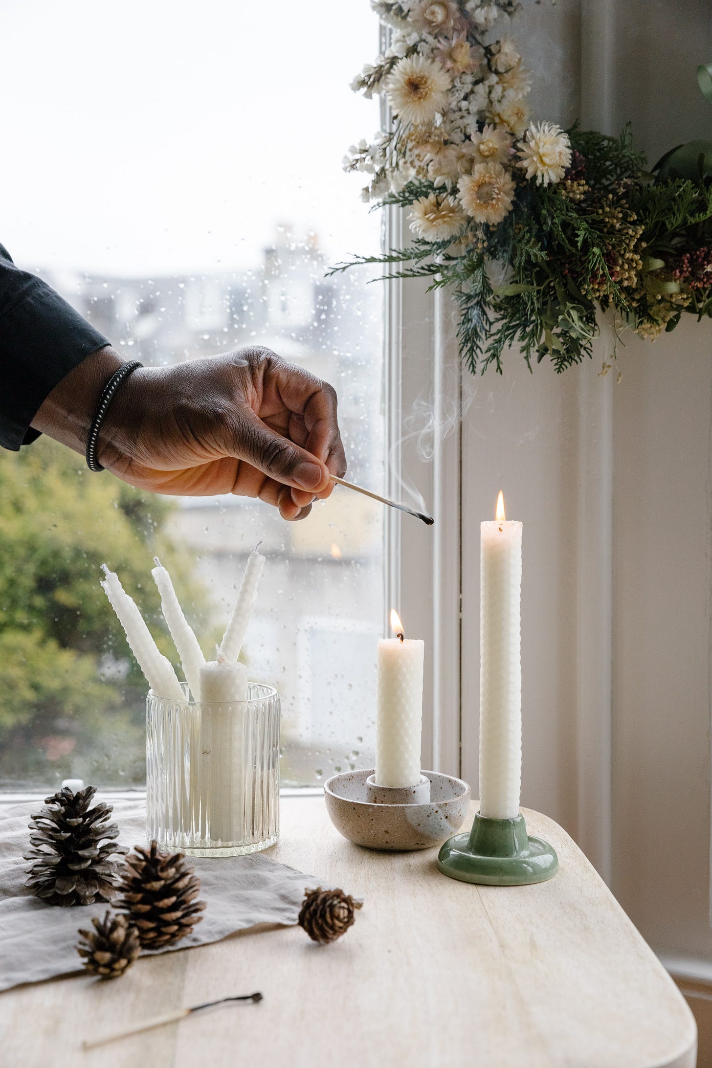 A man's hand is lighting a  candle in front of a rainy window.