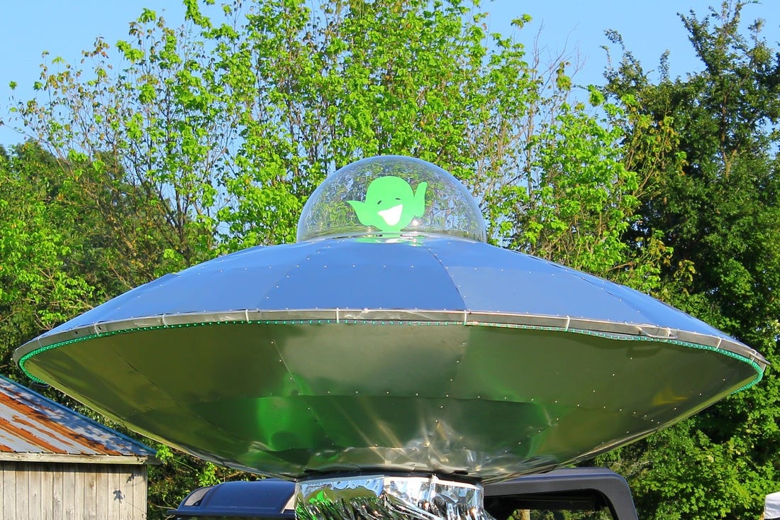 A small green cardboard cutout of an alien face sits inside a recreated flying alien saucer.