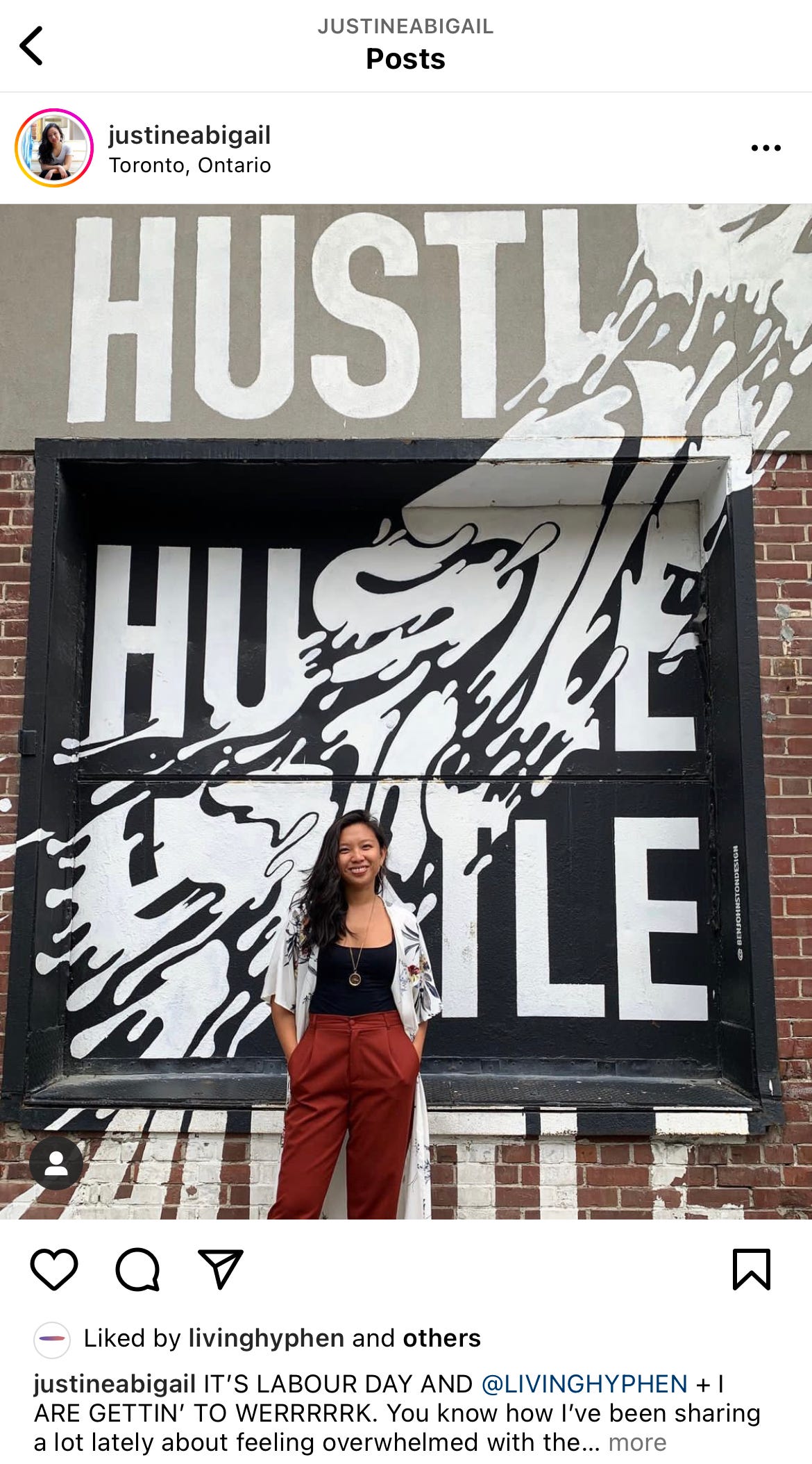 Justine standing in front of a mural that reads "HUSTLE HUSTLE HUSTLE"