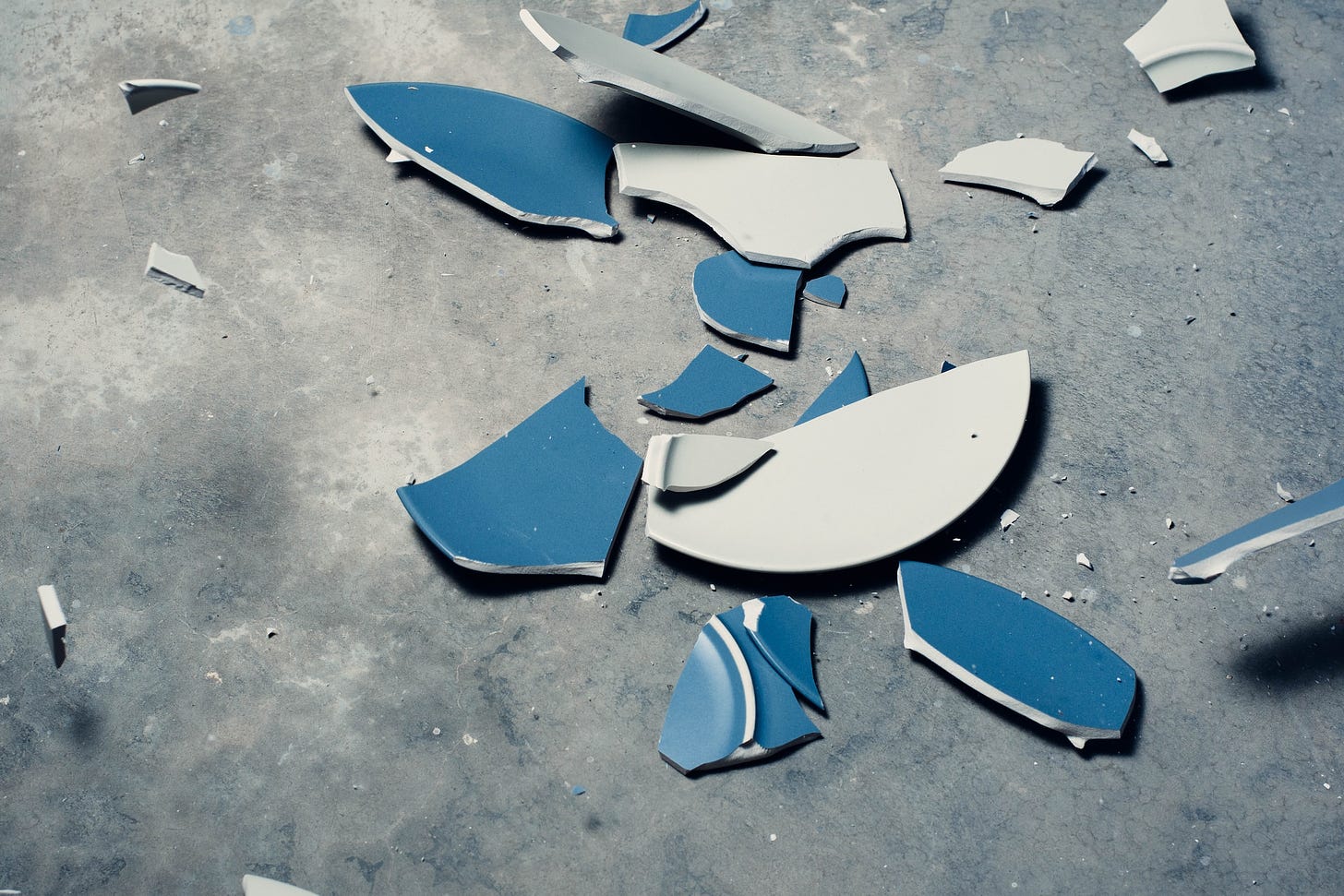 A blue plate shattered on a grey floor.