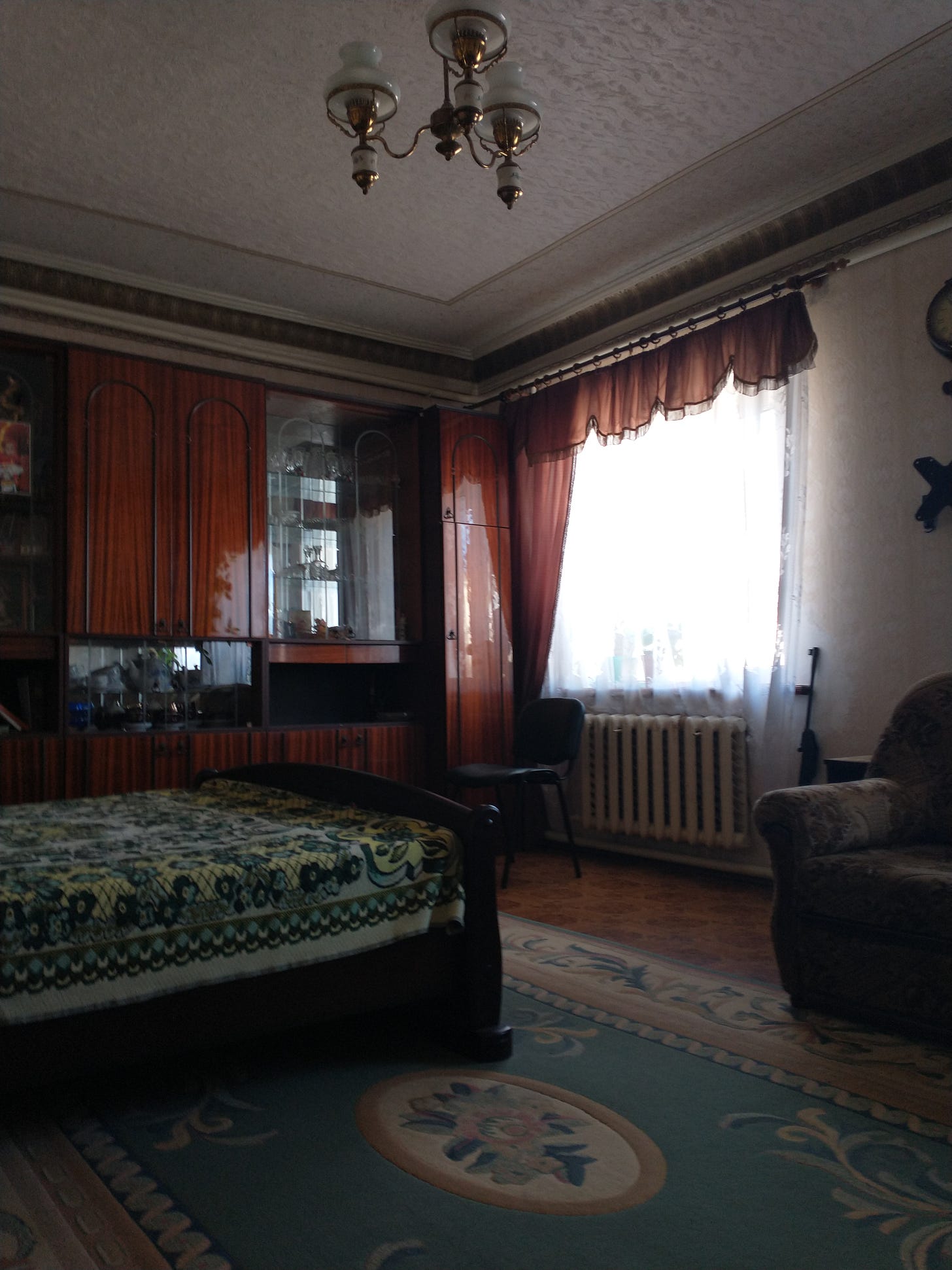 Luda's bedroom. Traditional Ukrainian furnishings and decorative elements adorn a well-lit room. She keeps a loaded rifle by window in case of trouble. 