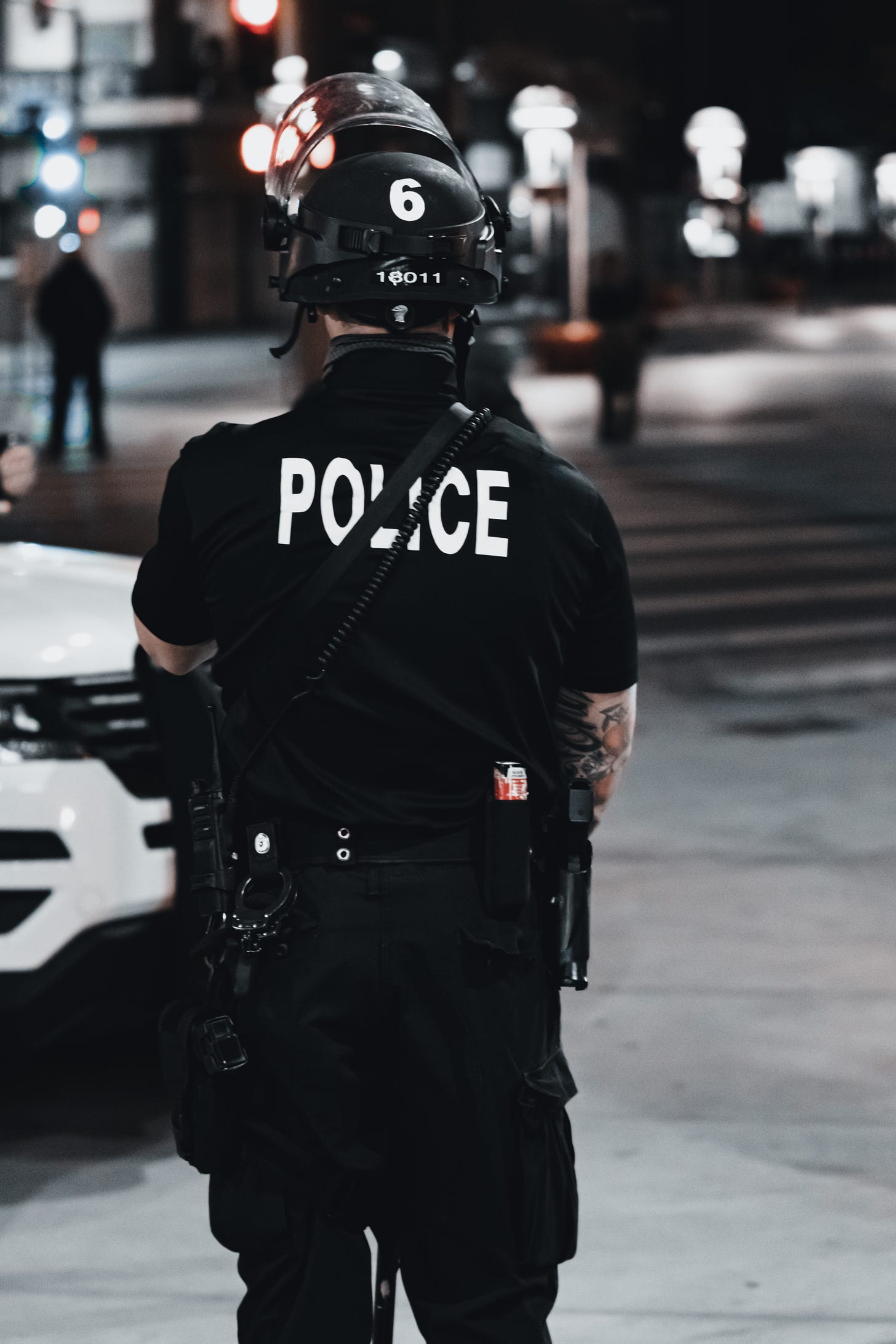 a police officer wearing a helmet facing away from the camera on a dark city street