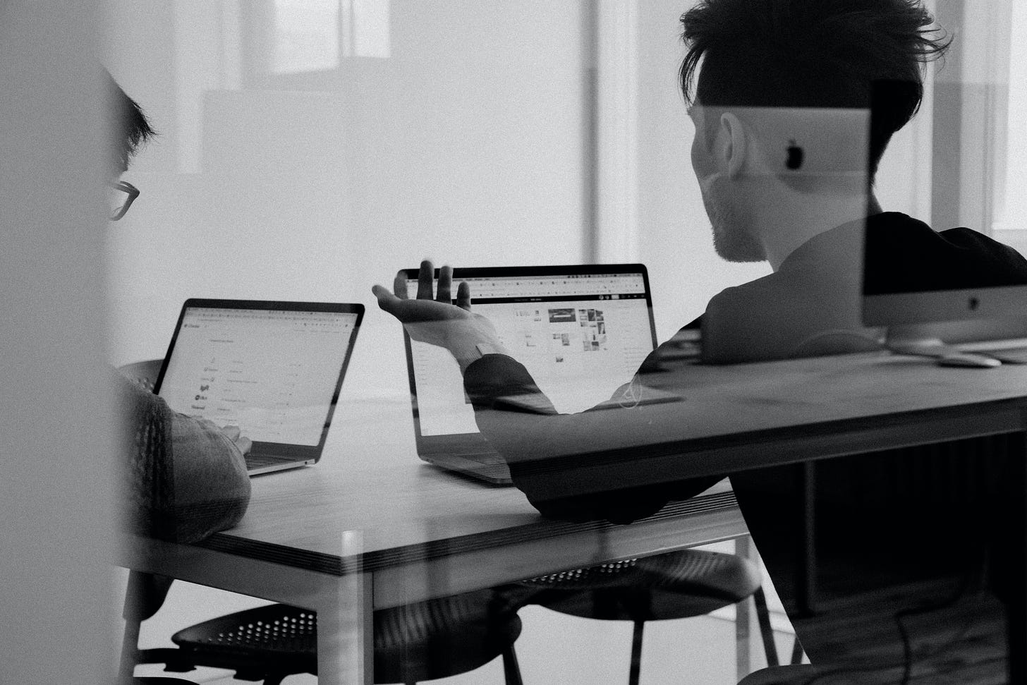 Two people discussing over their computers at a desk