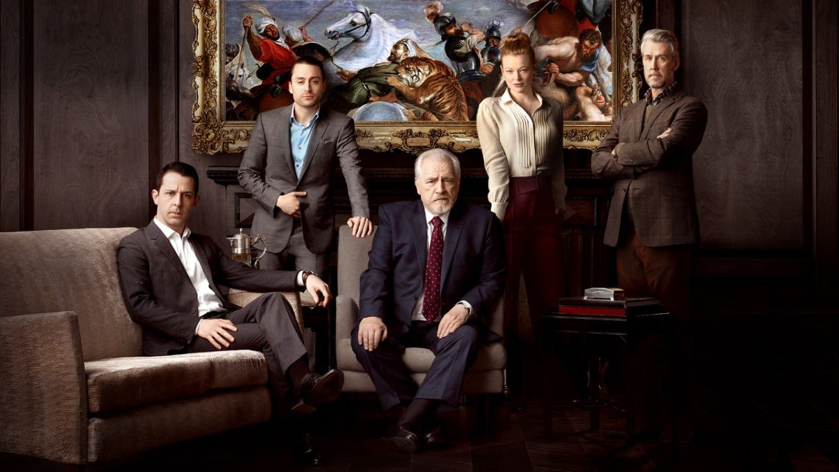 Five white people (three middle aged men, a young woman, and an old man) pose for the camera wearing formal attire in a fancy living room, in front of a classic painting depicting war
