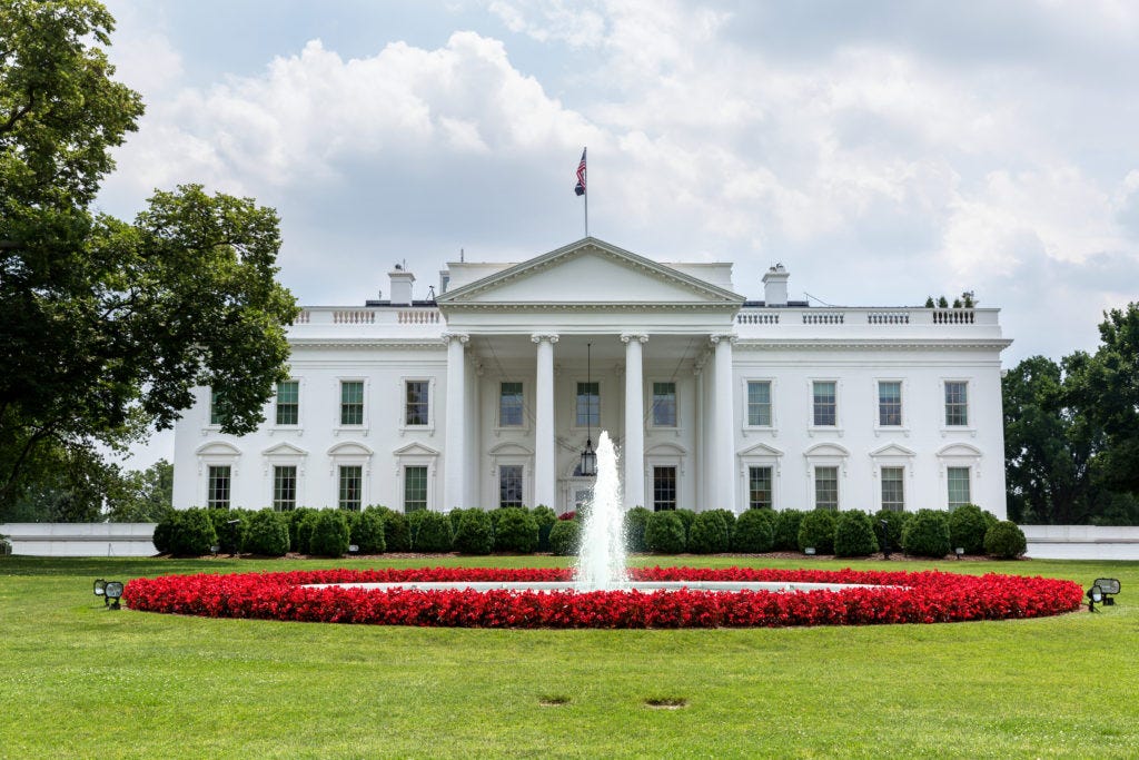 A white house with a fountain in front of it

Description automatically generated