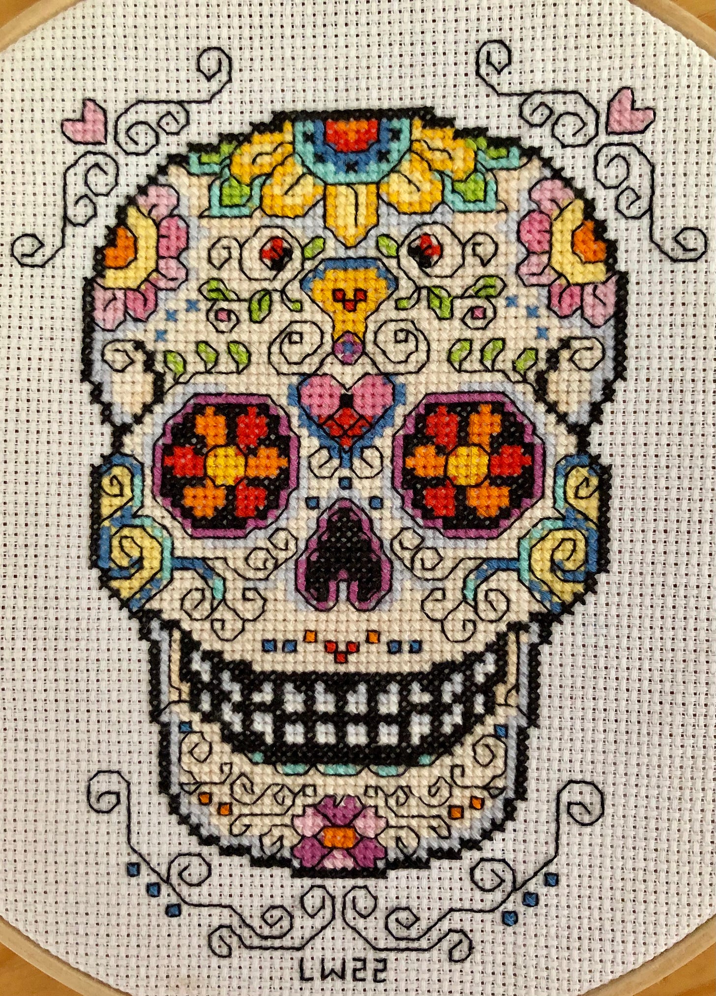 A cross-stitched image of a Day of the Dead sugar skull