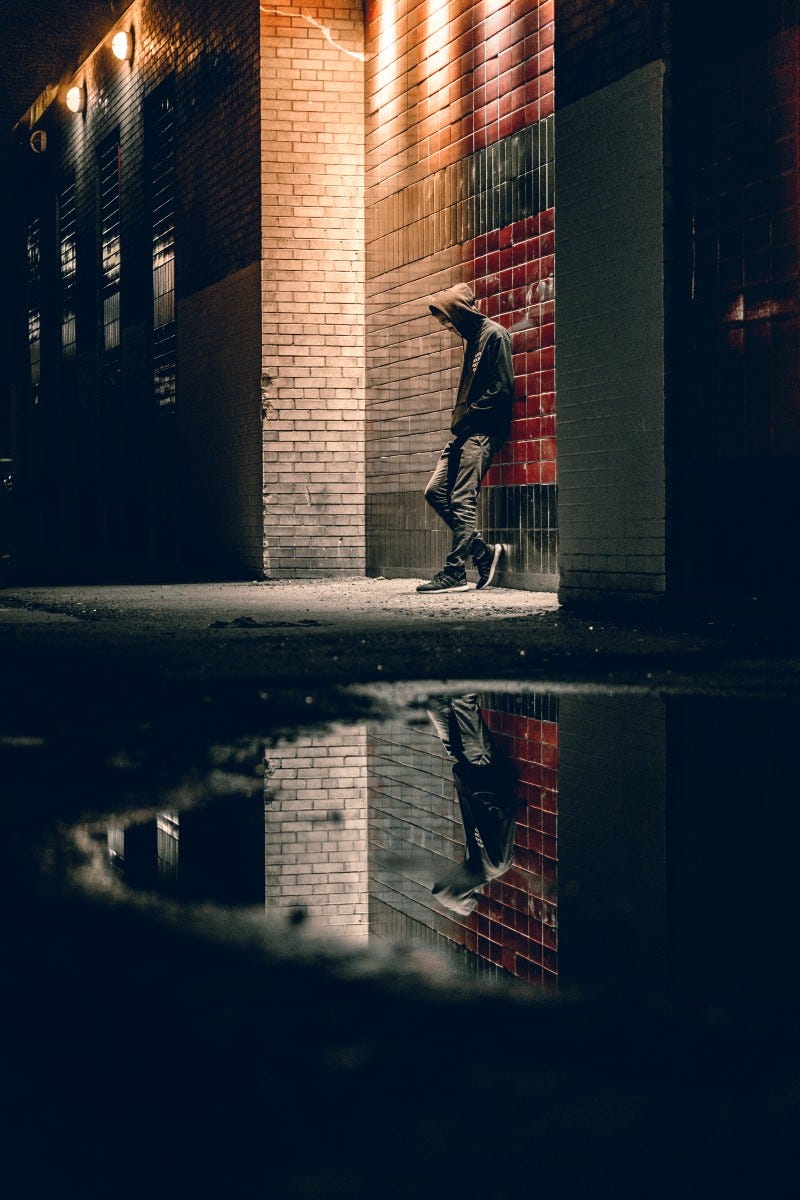 man in hoodie leaning against brick wall