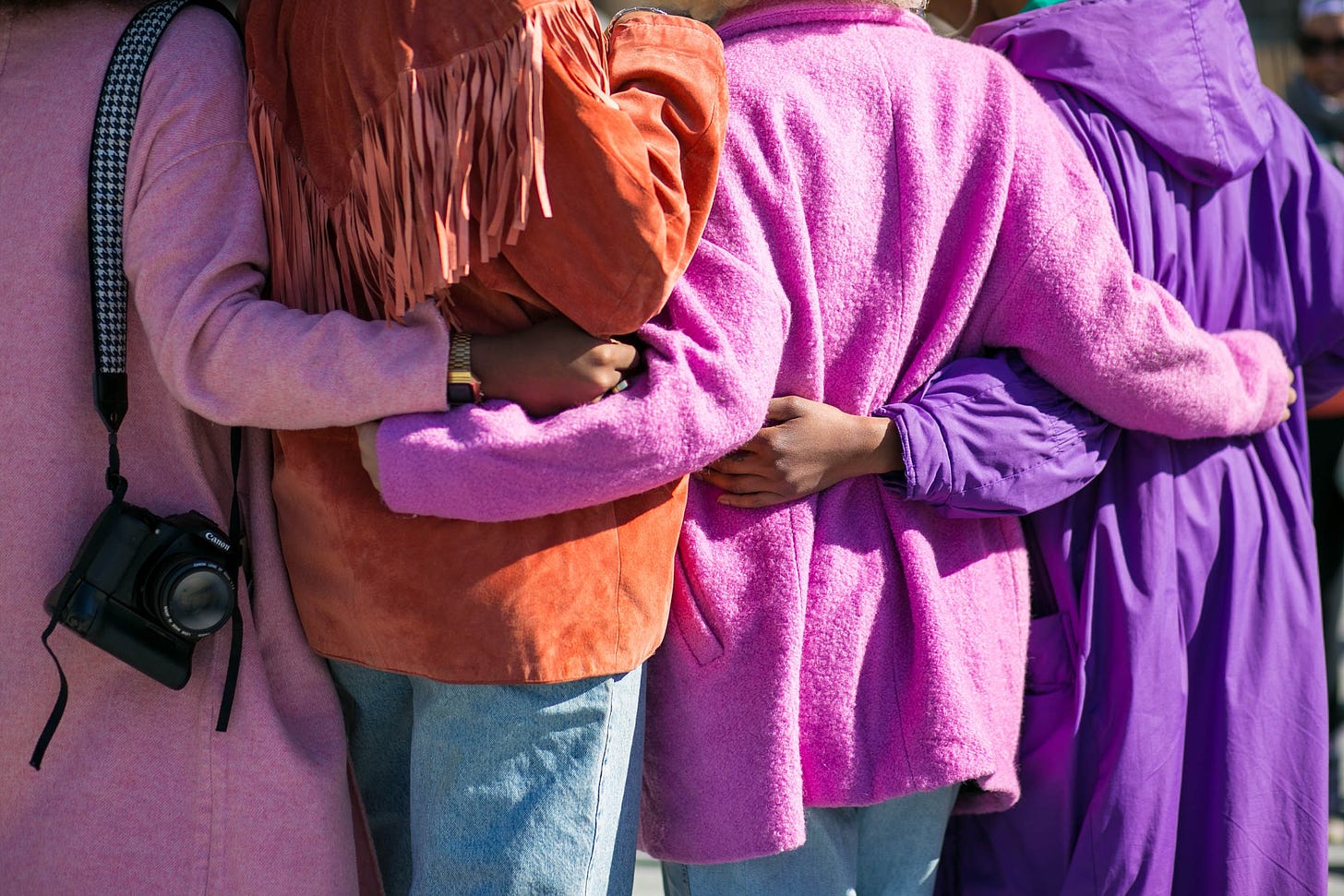 A group of four people wearing colourful jackets stand arm in arm
