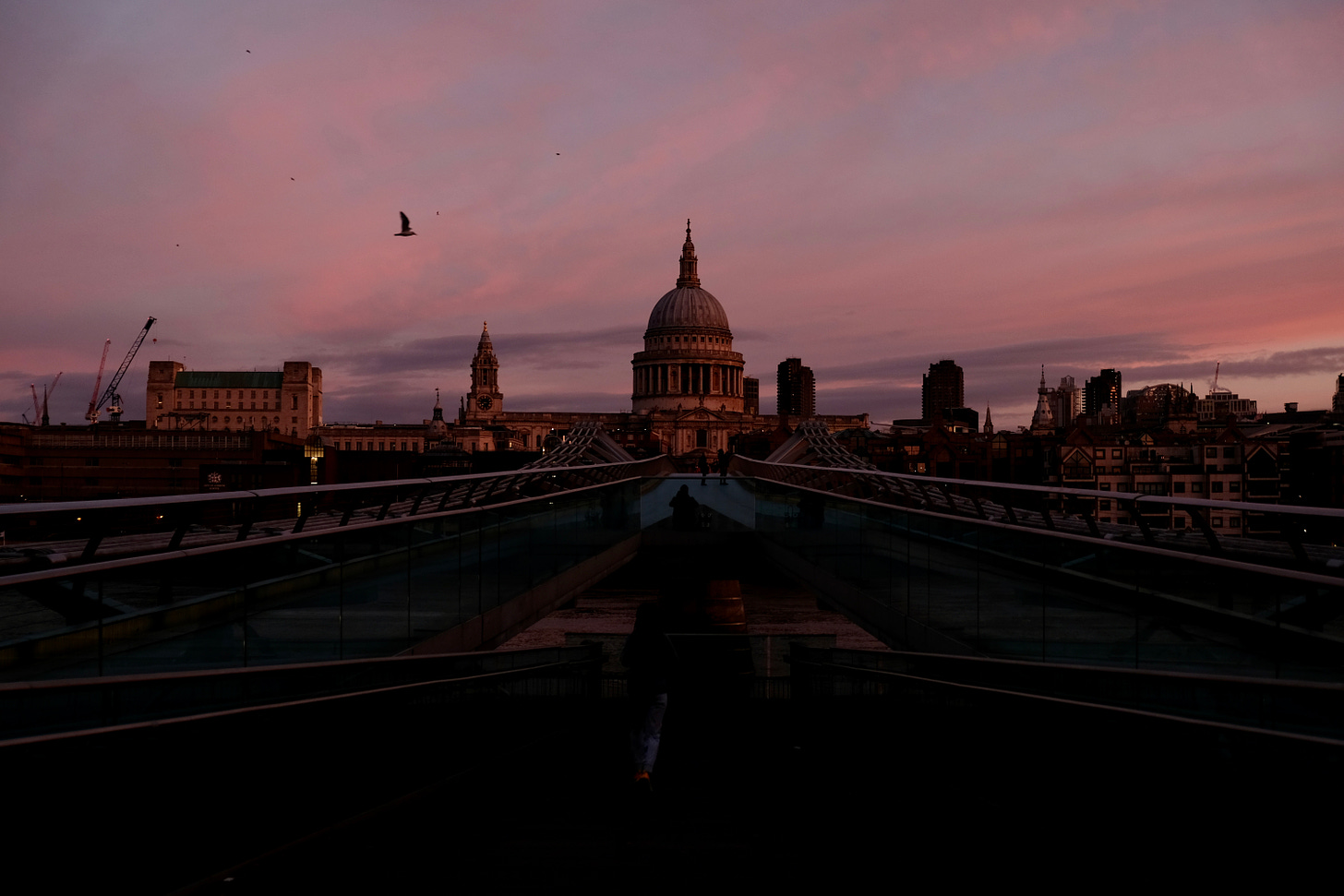 A pink and purple sunrise in London over St. Paul's Cathedral, with a view of Millennium Bridge in the foreground.