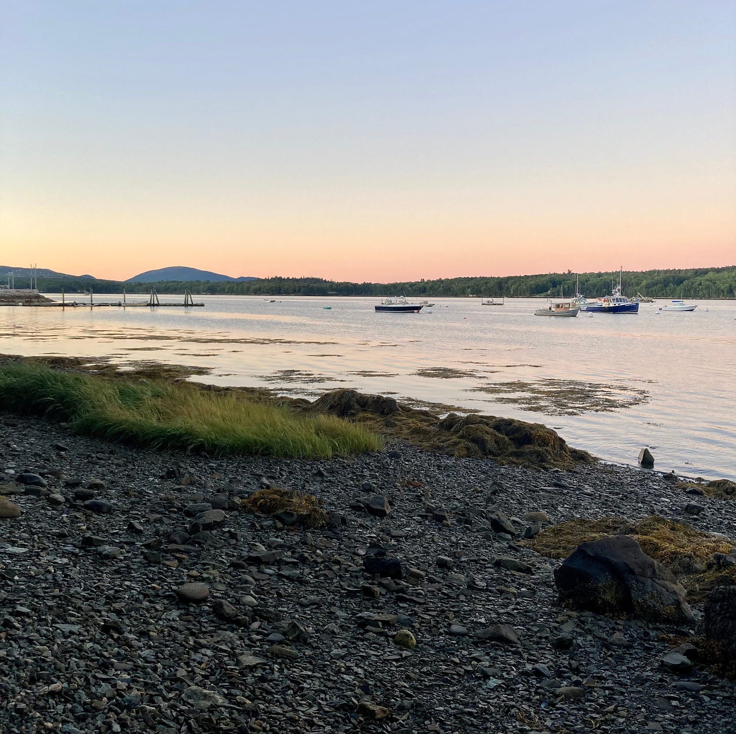 Sunrise on a rocky beach. There are lobster boats clustered in the water.