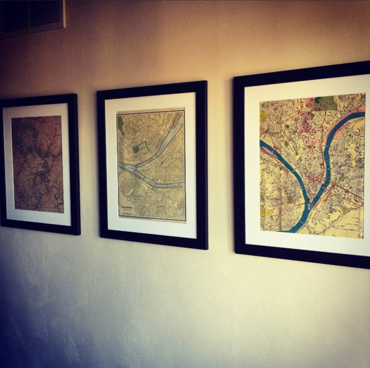 A wall with three framed maps of Pittsburgh's rivers and surrounding areas
