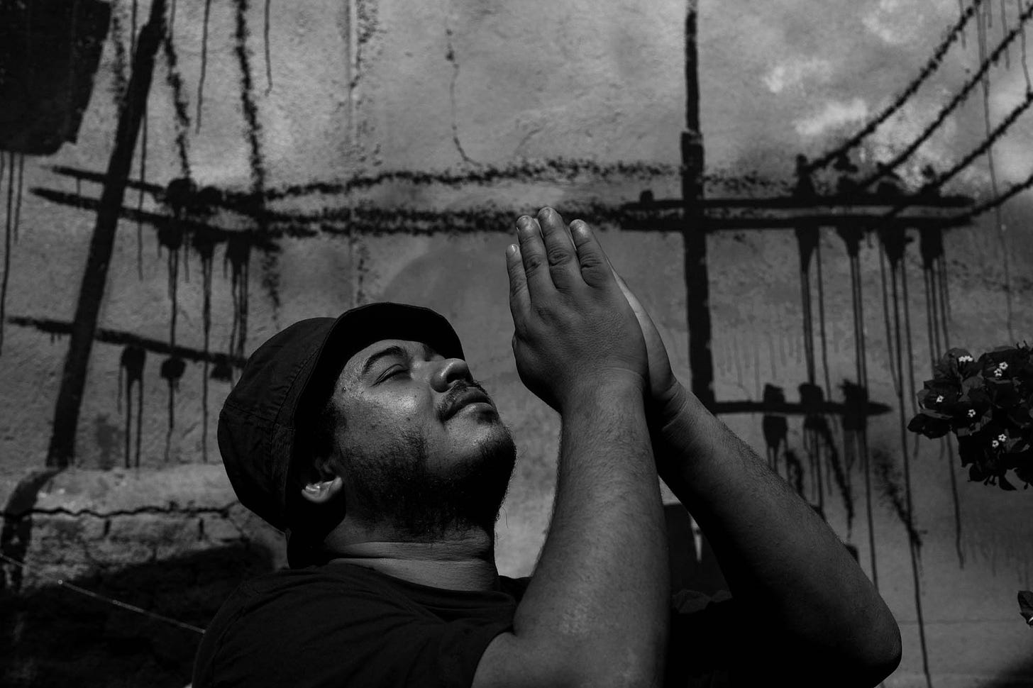 Fotografia em preto e branco mostra Thiago Vinicius com as mãos levantadas para o céu, em prece.