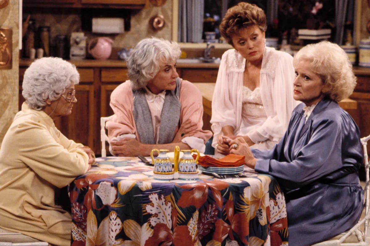 Four white women sit around a kitchen table in their nightgowns