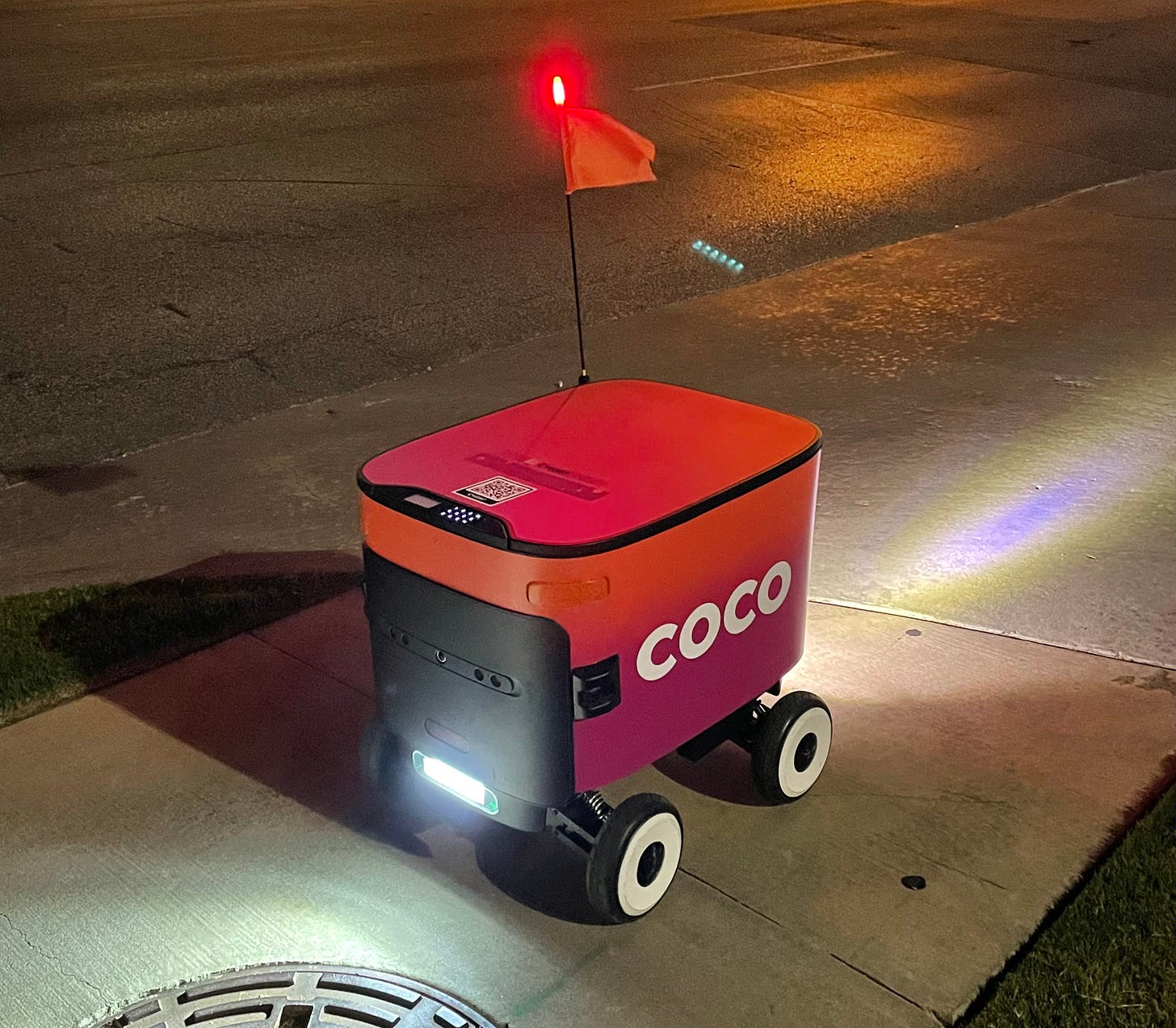 A small red delivery robot on a sidewalk
