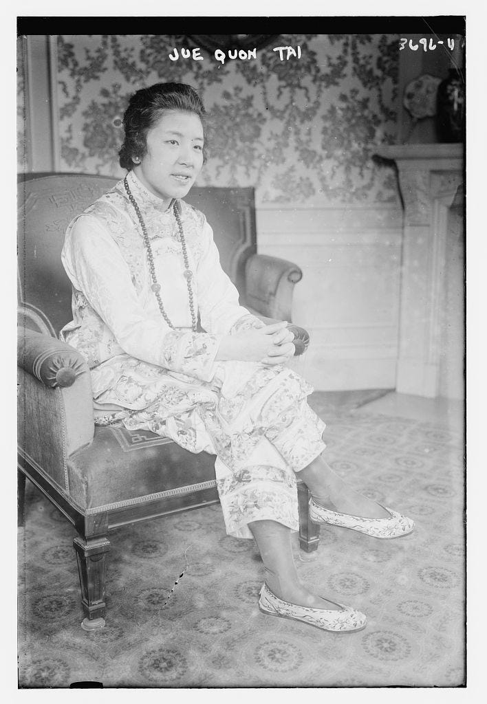 Jue Quon Tai in 1915, she sits in an arm chair in a traditional Chinese silk pantsuit with slippers