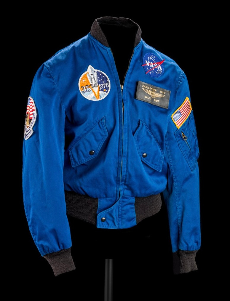 A deep blue NASA flight jacket with patches that indicate a 1978 Shuttle Mission, an American Flag, and a name patch that says "Sally Ride." 