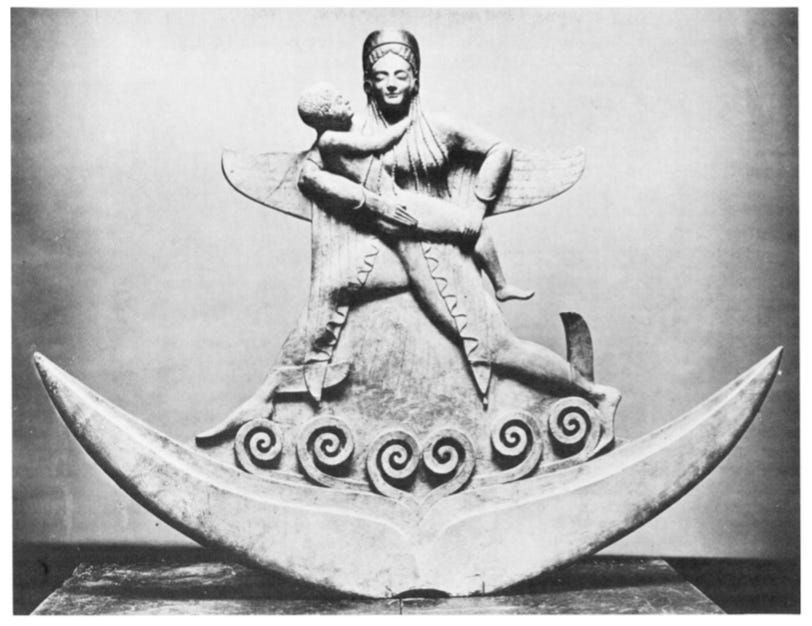 A black and white photo depicts a statue of a striding figure with wings cradling a smaller human figure in their arms.  The winged figure stands on a crescent moon with waves at their feet.