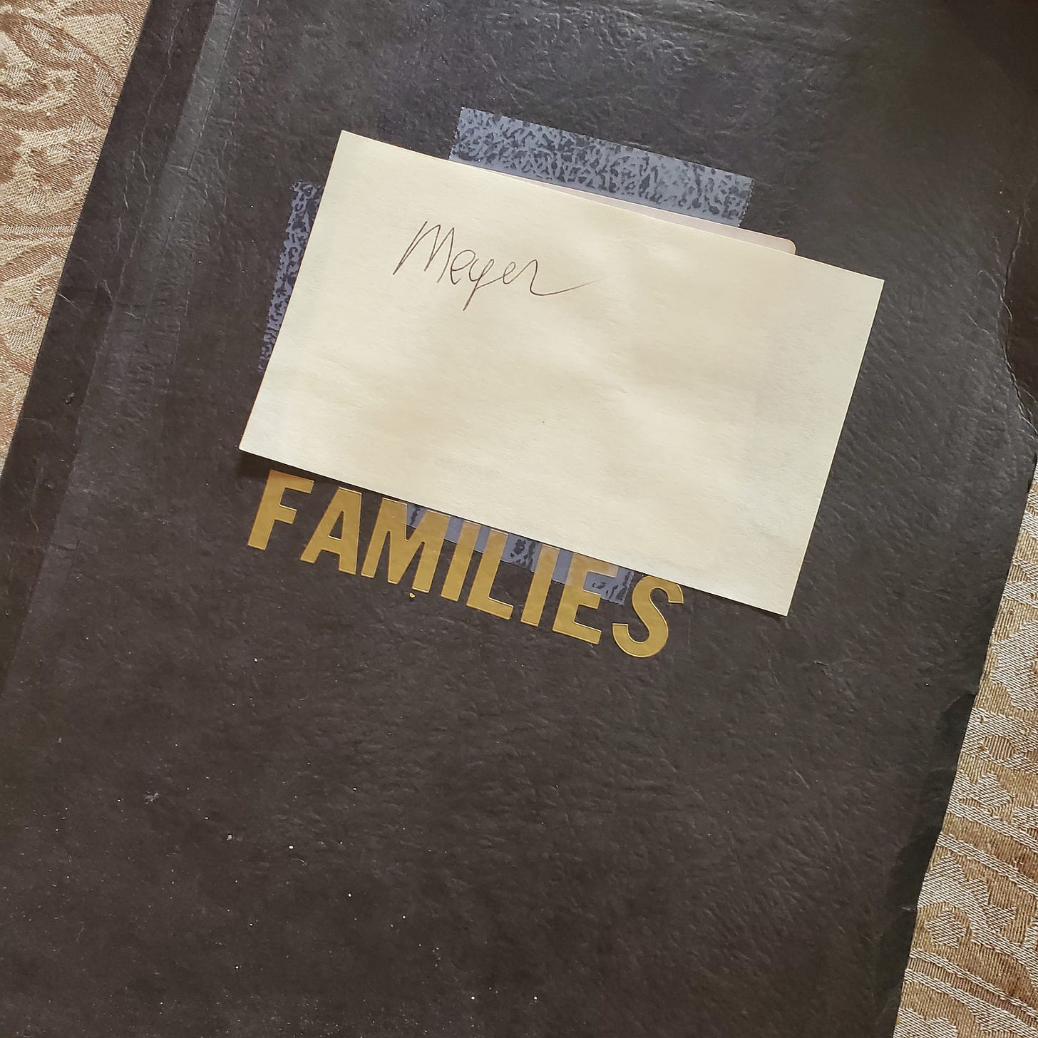 A black binder with "Meyer" written on a post-it note over a gilt printing of "Families." 