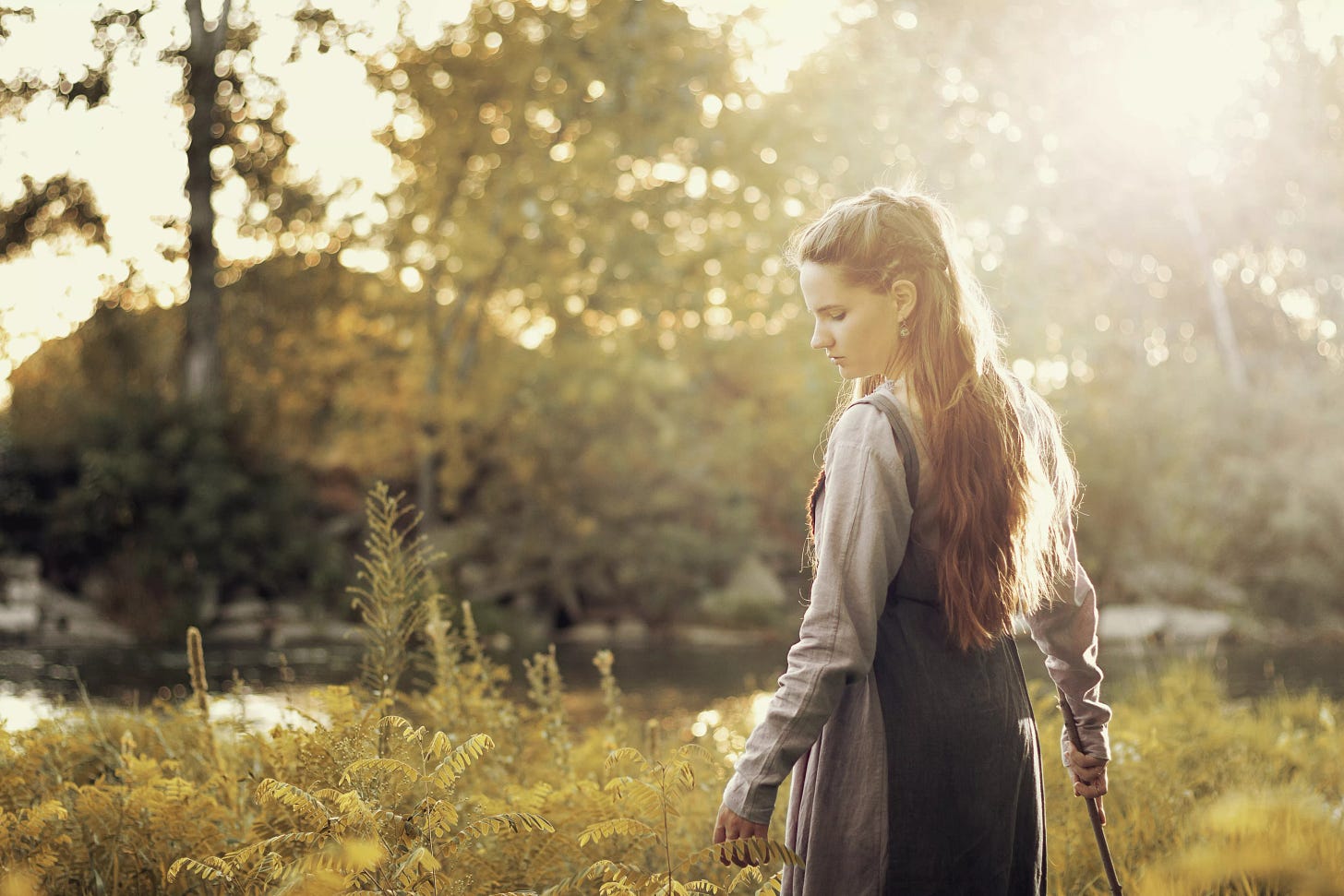 Young woman with long hair in period viking costume looks down, turning, outdoors and sunlit