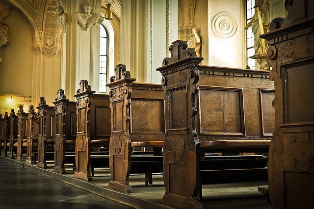 View of ornate, wooden pews down one side of church aisle.